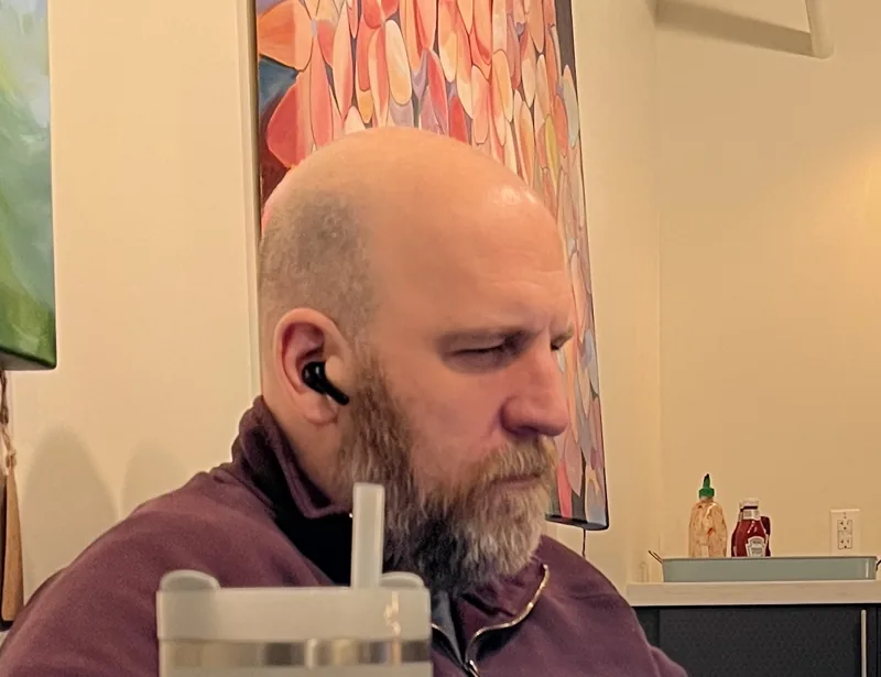 Jim Hollis working at a laptop in a coworking space, wearing an earbud